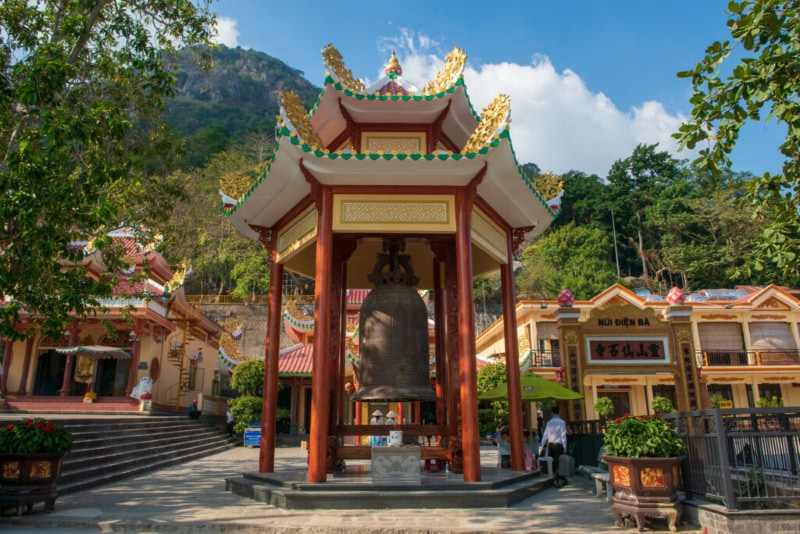 The large temple bell stands prominently in front of the temple.